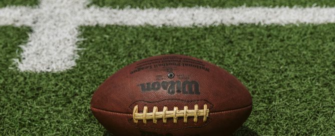 A brown American football lying on green turf with white field markings