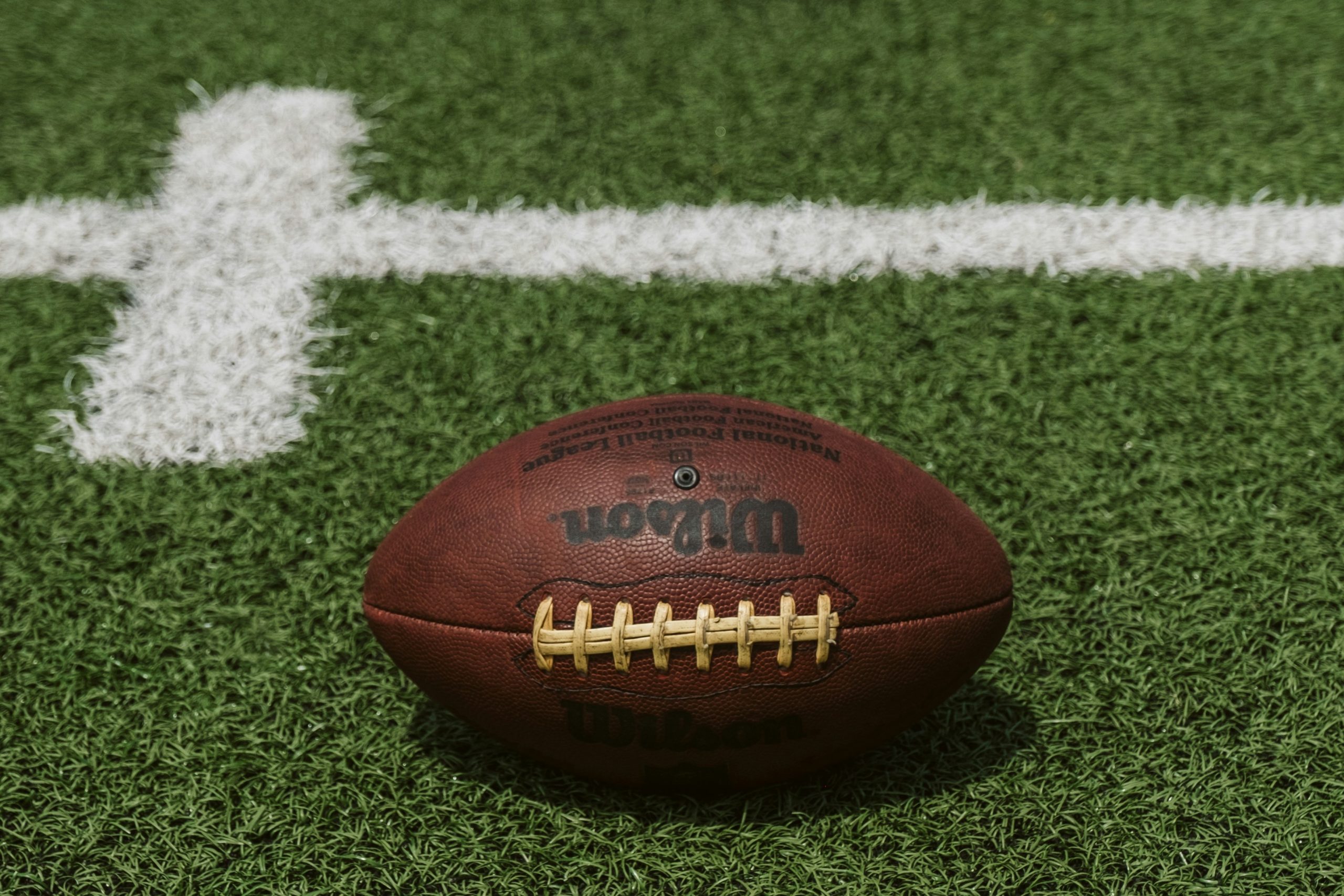 A brown American football lying on green turf with white field markings